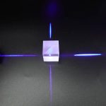 Prisma cúbico transparente com feixes de luz azul dispersos em diferentes direções, mostrando dispersão de luz através do prisma.