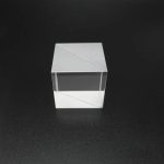 Cubo de acrílico transparente com linhas diagonais, usado para dispersão de luz, visto de cima com fundo preto.