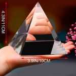 Pirâmide de cristal transparente com reflexos, medida 4.3 polegadas de altura e 3.9 polegadas de base, segurada na mão com fundo desfocado.