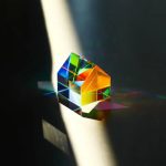 Prisma pentagonal de vidro transparente dispersando luz solar em cores do arco-íris, criando um espectro de cores na superfície.