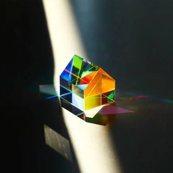 Prisma pentagonal de vidro transparente dispersando luz solar em cores do arco-íris, criando um espectro de cores na superfície.
