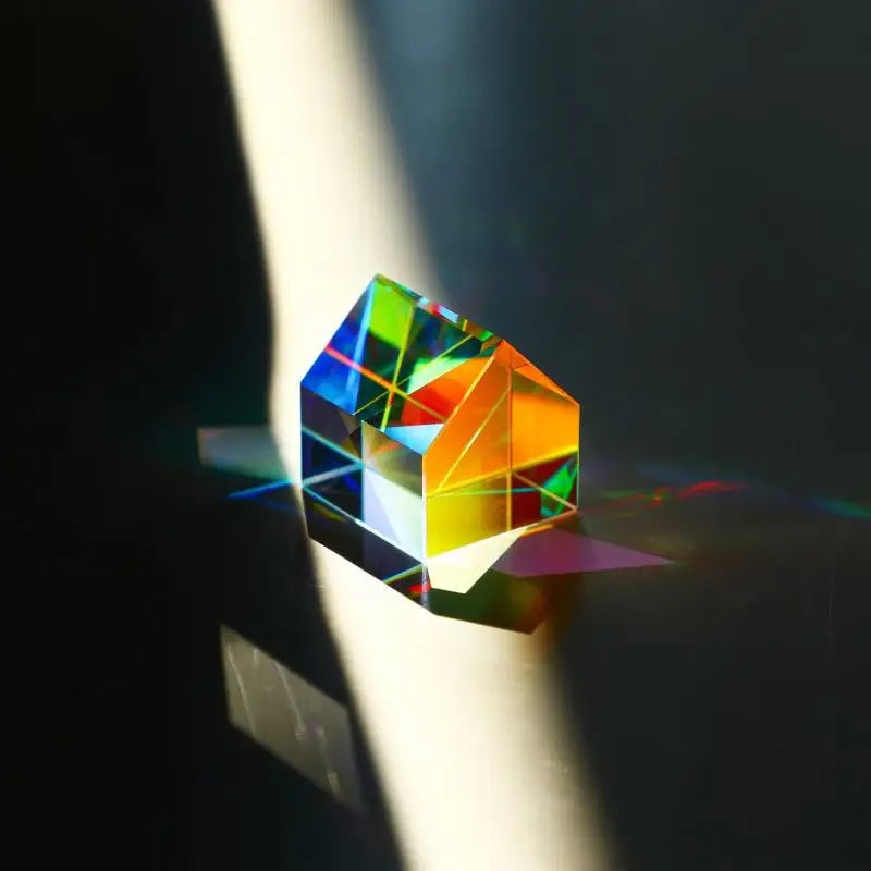 Prisma pentagonal de vidro transparente dispersando luz solar em cores do arco-íris, criando um espectro de cores na superfície.