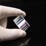 Prisma retangular dicroico com várias faixas de cores refletidas e transmitidas, usado em experimentos de óptica para separar luz de diferentes comprimentos de onda.