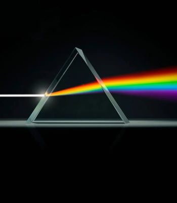 Prisma triangular de cristal dispersa luz branca em um espectro de cores vibrantes, com fundo escuro.