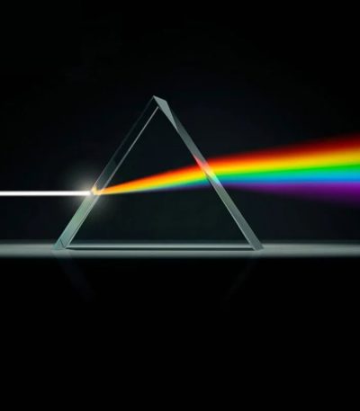 Prisma triangular de cristal dispersa luz branca em um espectro de cores vibrantes, com fundo escuro.