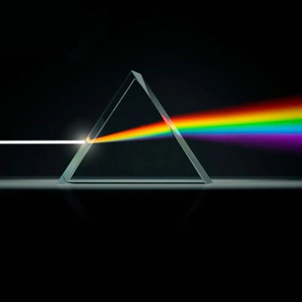 Prisma triangular de cristal dispersa luz branca em um espectro de cores vibrantes, com fundo escuro.