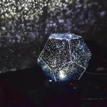 Projetor de constelações em forma de diamante com luzes brilhantes projetadas na parede escura.