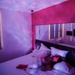 Céu estrelado projetado no teto e paredes do quarto, criando ambiente relaxante com luzes coloridas e estrelas brilhantes.