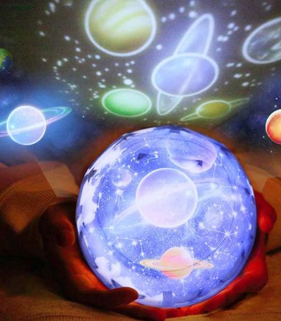 Mãos segurando esfera com projeção de planetas e estrelas, luzes coloridas de galáxia e sistema solar.