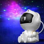 Robô projetor com forma de astronauta, projetando estrelas e galáxias coloridas no teto, ideal para ambientes educativos e de lazer.