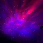 Projeção de estrelas coloridas no teto com tons de roxo, azul e rosa, criando efeito de céu estrelado.