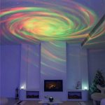 Projeção de luzes coloridas de uma nebulosa no teto de uma sala com decoração moderna e sofá.