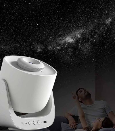 Projetor de estrelas branco a projetar o céu noturno na parede, com uma pessoa a observar e uma criança deitada na cama, ambiente escuro.