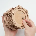Pessoa a montar uma caixa de música em madeira com detalhes mecânicos visíveis, usando uma ferramenta para ajustar uma peça no centro do dispositivo.