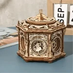 Caixa de música em madeira com detalhes intricados, mostrada numa mesa, com fundo de parede e outros objetos ao lado.
