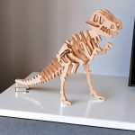 Modelo de dinossauro T-Rex em peças de madeira, vista lateral, com detalhes do esqueleto e cabeça, sobre uma superfície branca.