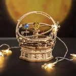 Modelo de puzzle 3D do globo celeste com planetas e órbitas, iluminado com luzes decorativas, sobre fundo escuro com uma imagem do espaço ao fundo.