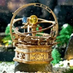 Modelo de globo solar mecânico com planetas coloridos em movimento, detalhes em madeira e estrutura circular, sobre fundo de neve e árvores verdes.