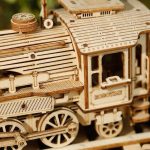 Detalhe de uma locomotiva de madeira em puzzle 3D, com rodas, carruagem e detalhes intricados, vista de perto.
