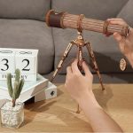 Telescópio de madeira com tripé ajustável, detalhes finos e cordão decorativo pendurado na extremidade.