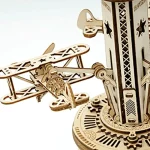 Detalhe de uma réplica de avião em madeira do puzzle 3D, com partes articuladas e detalhes intricados, junto a uma estrutura de torre de madeira.