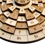 Peças de madeira numeradas de 1 a 50, dispostas em círculos concêntricos, usadas em jogo de estratégia matemática.