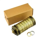 Cryptex com cilindro de letras e dois anéis, um dourado e um prateado, ao lado de uma caixa de papelão.