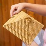 Quebra-cabeças em forma de pirâmide feito de peças de madeira, com várias camadas e detalhes intricados, sendo manipulado por uma pessoa.