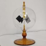 Radiómetro de Crookes com esfera de vidro transparente, hélices internas em movimento, base de suporte de cor âmbar, usado para demonstrar radiação de luz.