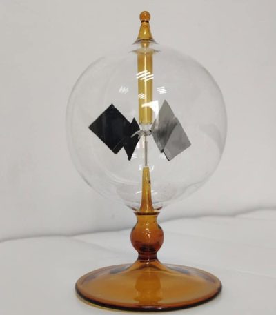 Radiómetro de Crookes com esfera de vidro transparente, hélices internas em movimento, base de suporte de cor âmbar, usado para demonstrar radiação de luz.