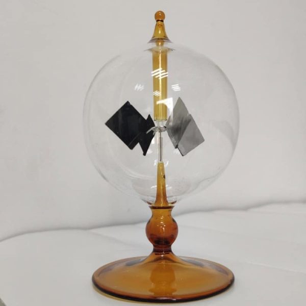 Radiómetro de Crookes com esfera de vidro transparente, hélices internas em movimento, base de suporte de cor âmbar, usado para demonstrar radiação de luz.