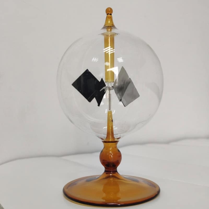 Radiómetro de Crookes com esfera de vidro transparente, hélices internas em movimento, base de suporte de cor âmbar, usado para demonstrar radiação de luz.