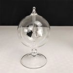 Radiómetro de Crookes em vidro transparente com lâmpada de plasma visível no interior, apoiado numa base de vidro.