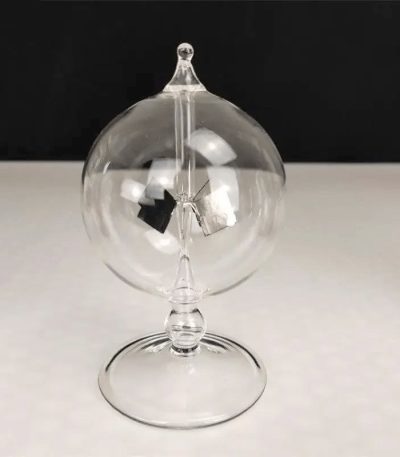 Radiómetro de Crookes em vidro transparente com lâmpada de plasma visível no interior, apoiado numa base de vidro.