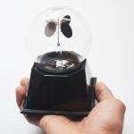 Radiómetro meteorológico com esfera de vidro transparente, hélices metálicas e base preta, usado para medir radiação solar.