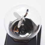 Radiómetro meteorológico com asa de vento de metal, visível através de uma esfera de vidro, colocado sobre uma base preta.