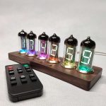 Seis tubos Nixie com números visíveis, cada um com iluminação colorida, montados numa base de madeira, com controlo remoto ao lado.