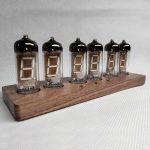Seis tubos Nixie com dígitos visíveis, montados numa base de madeira, formando um relógio digital vintage.