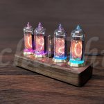 Quatro tubos Nixie iluminados com cores diferentes, montados numa base de madeira, exibindo números e símbolos.