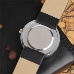 Relógio com pulseira de couro bege e preta, mostrador de aço inoxidável, vista de trás, detalhes do mecanismo e acabamento.