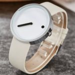 Relógio com mostrador minimalista, ponteiro único preto, caixa metálica e pulseira de couro branco.