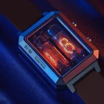 Relógio Nixie com tubos de exibição em vidro, iluminados em tons quentes, com caixa metálica e pulseira de couro escura.