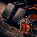 Relógio Nixie com tubos de exibição de números em vidro, detalhes internos visíveis, com cabos de energia, em fundo escuro com brilho de partículas.