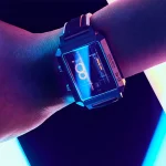 Relógio Nixie com visor digital iluminado em tons azuis e roxos, exibindo números e gráficos, usado no pulso de uma pessoa.