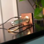 Relógio Nixie com tubo de vidro visível, exibindo a hora em números digitais azuis, com base de madeira e cabos conectados.