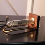 Relógio Nixie com tubo de vidro visível, base de madeira e cabos conectados, exibindo números fluorescentes.