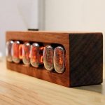 Relógio Nixie com tubos de vidro em caixa de madeira, mostrando a luz laranja dos dígitos em diferentes ângulos.