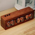 Relógio Nixie com tubos de vidro exibindo números laranja, montado numa base de madeira, com botões de controlo no topo esquerdo.