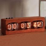 Relógio Nixie com caixa de madeira, exibindo horas, minutos e segundos em tubos de néon vintage, com botões de controlo no topo, numa superfície de madeira.