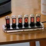 Seis tubos Nixie exibindo os números 1, 7, 2, 0, 1, 2 em cores laranja e vermelho, colocados numa base de acrílico transparente sobre uma mesa de madeira.
